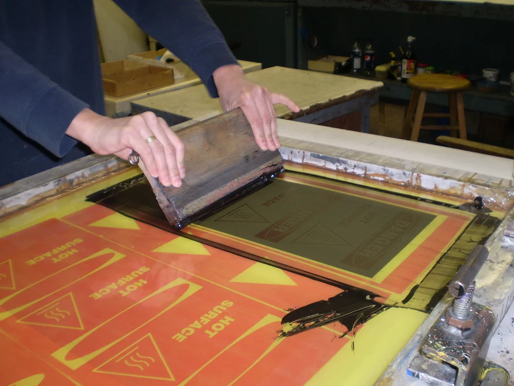 Hand pulling a squeegee across a silkscreen to print labels